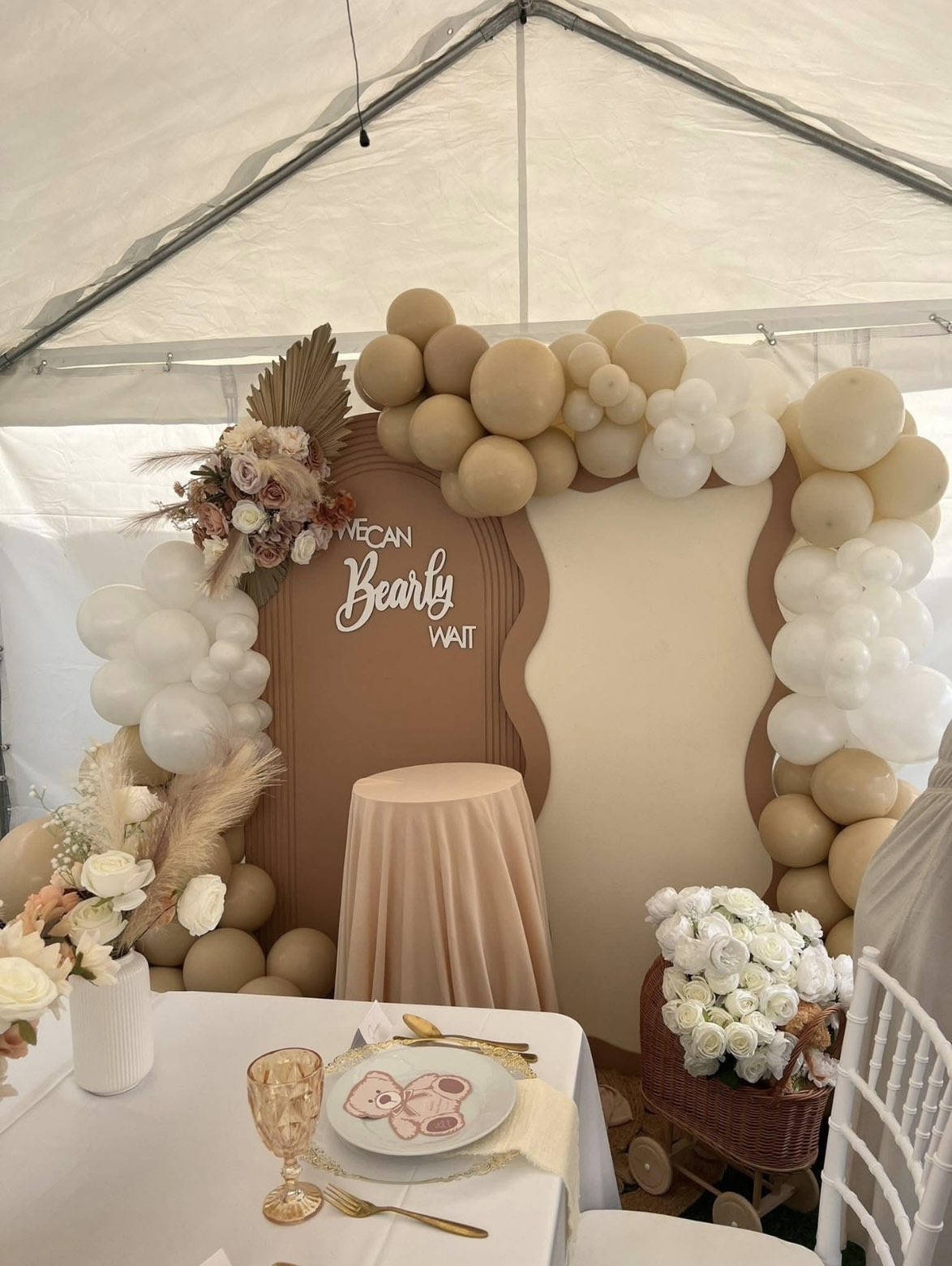 Baby shower marquee setup with neutral balloon arch, floral arrangements and elegant table setting