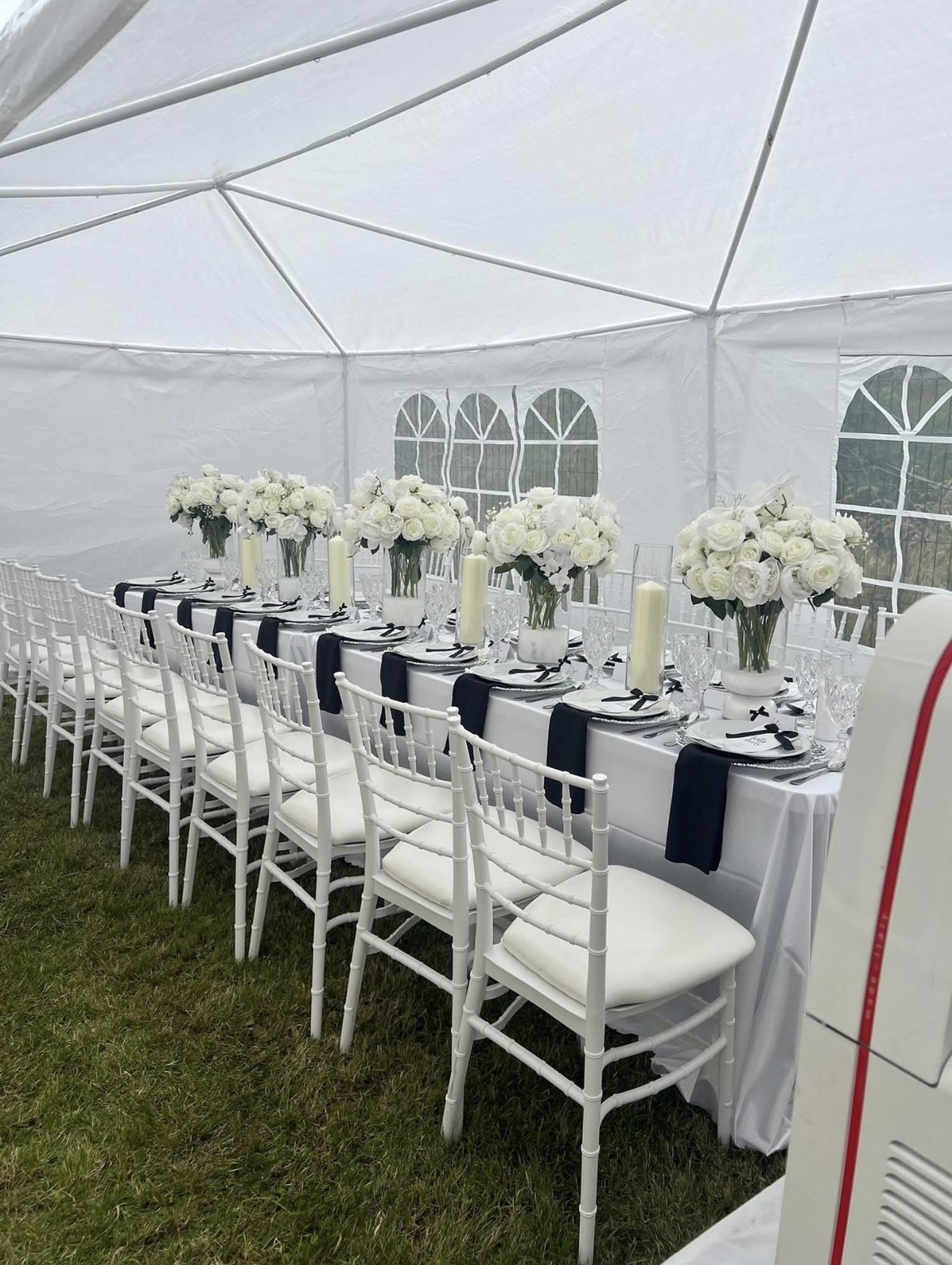 Long wedding table with white chiavari chairs, navy sashes and white floral arrangements